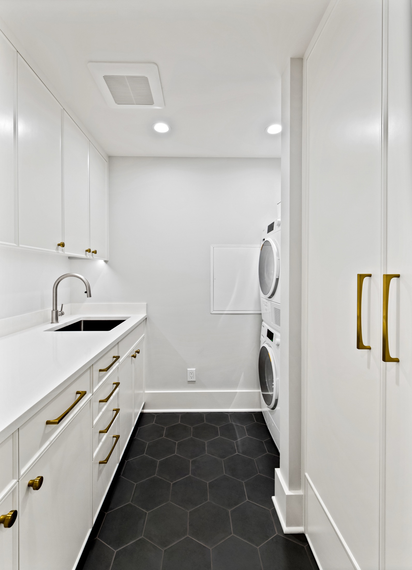 Laundry room with white cabinets and dark hexagonal floor tile