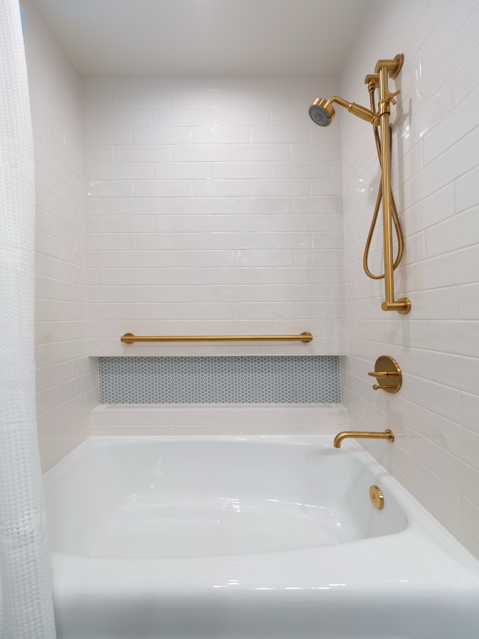 Brass shower fixture above the white tiled bathtub