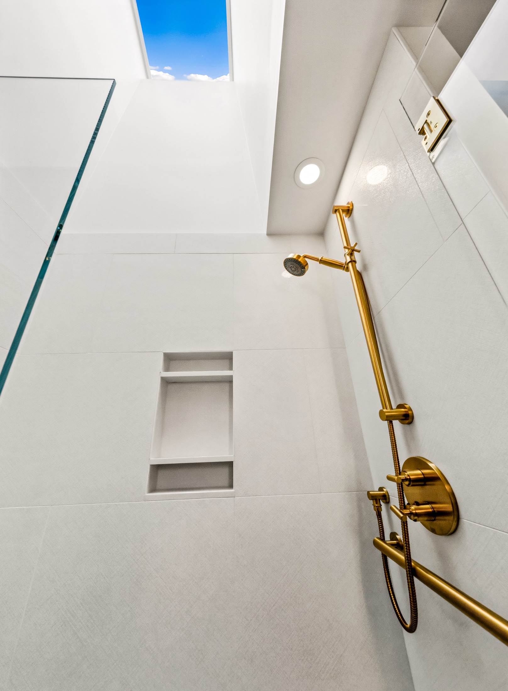 Brass rainfall shower fixture against white tile