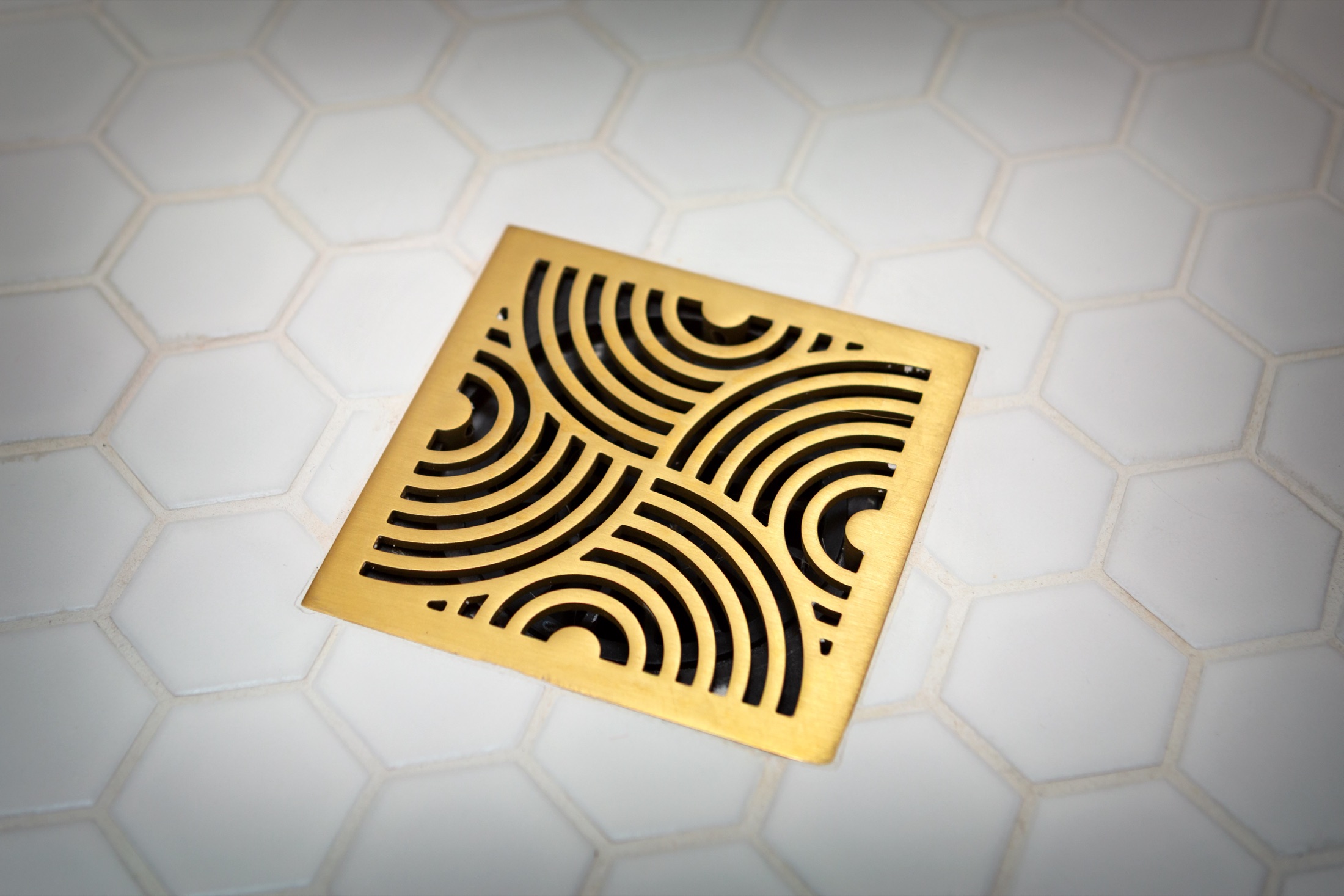 Decorative brass drain set into white hexagonal floor tile