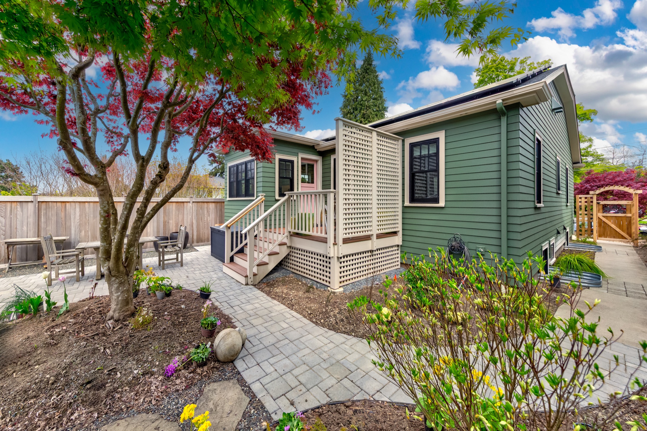 Green home addition beside mature landscaping and stone patio